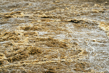 Smudged water flows profusely. River water flowing profusely. Flood waters rushing down river after storm flows through. Turbulent river dam. Water turbulence of river due to dam. Water Nature Texture