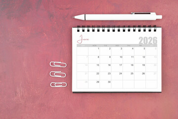 Desk calendar for June 2026 and pen with paper clips on red table, Flat lay.