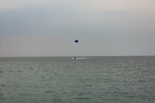 Parasailer glides above the ocean, towed by a boat. Water sports activity.