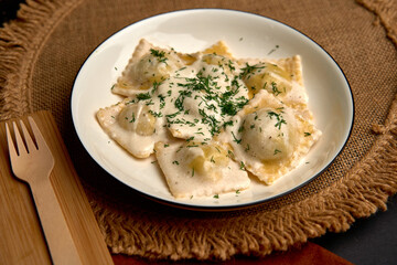 Delicious Plate of Homemade Ravioli Topped with Creamy Sauce and Fresh Herbs Served on Rustic Tableware for a Hearty Italian Meal
