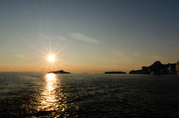 Summer on Greenland's west coast reveals icy fjords, glowing midnight sun, whales gliding through cold waters, and colorful villages nestled among towering icebergs.