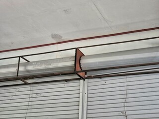 Close up of a metallic industrial rolling shutter mechanism with rusted support frame indoors