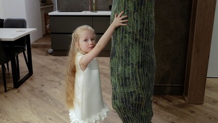 Smiling child in white dress delicately touching netted christmas tree, expressing festive wonder and gentle holiday anticipation