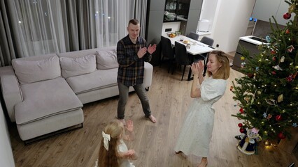 Festive family moment showcasing young girl clapping near sparkling christmas tree, sharing warmth and happiness in decorated living room during holiday gathering