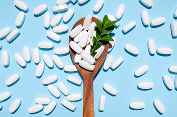 White tablets, vitamins, pills and green leaf in wooden spoon on blue background top view. Medical pharmaceutical background, health concept, organic dietary supplements, self care