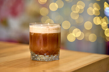 A delicious cocktail in a crystal glass, elegantly placed on a wooden table, shimmering bokeh lights in the background create a festive atmosphere.