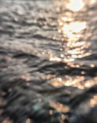 The reflection of the afternoon sun is golden orange on the surface of the river water in a blurry manner.