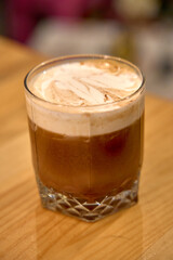 A Richly Brewed Coffee Drink with Creamy Foam Layering and Swirls, Presented in a Classic Short Glass for Instant Delight and Inviting Aroma