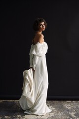 Elegant model in a flowing white gown posing gracefully in a minimalist studio setting with dark...