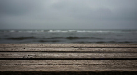 Empty wooden pier foreground with a moody, out-of-focus ocean background on a cloudy day.