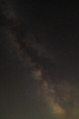 Against a dense field of stars and the glowing path of the Milky Way, a single streak cuts through—like a whispered wish flung across the dark canvas of eternity