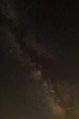 Against a dense field of stars and the glowing path of the Milky Way, a single streak cuts through—like a whispered wish flung across the dark canvas of eternity