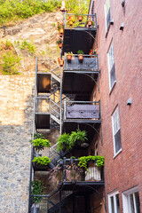 Tall brick building fire escape stairways and balconies with pots of plants in the Petit-Champlain sector of the old town seen during a summer morning, Quebec City, Québec, Canada
