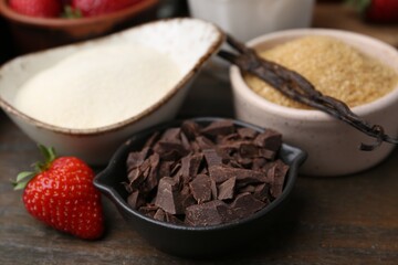 Different ingredients for panna cotta. Milk, sugar, vanilla, chocolate and strawberries on wooden table, closeup
