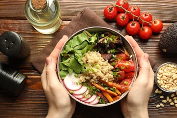 Healthy vegetarian food. Woman with delicious Buddha bowl and ingredients at wooden table, top view
