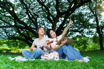 Naklejka premium Two Asian beautiful women sitting on picnic mat under the tree.