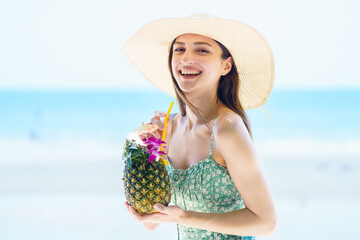Beautiful caucasian woman smiles to camera while holds a pineapple by the beach.