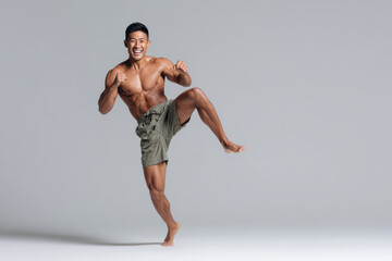 Fototapeta premium kickboxer in midaction with expressive smile displaying powerful right leg kick against clean solid background