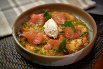 Deliciously Crafted Potato Dish Garnished with Smoked Salmon and Fresh Herbs, Perfectly Complemented by a Dollop of Creamy Sauce for a Culinary Delight
