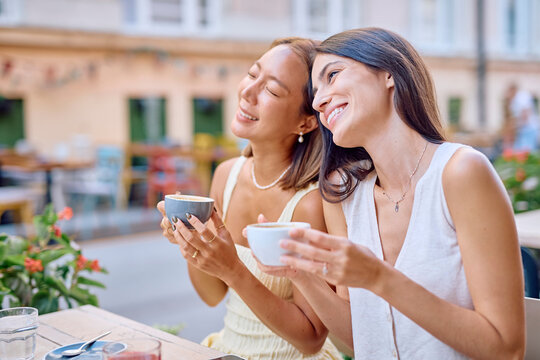 Two female friends are laughing and enjoying a coffee break together at an outdoor cafe, creating a cheerful and social atmosphere