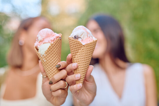 Two women enjoying ice cream cones while relaxing in a sunny park, sharing smiles and laughter during a warm summer day