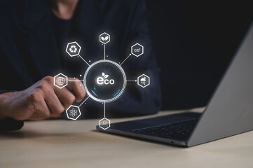 A person interacts with a digital eco-friendly concept hologram featuring sustainability and environmental icons above a laptop.