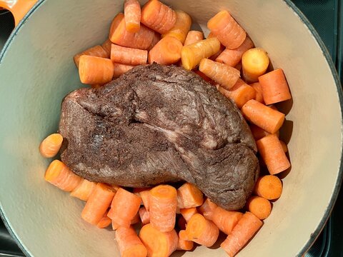 Seasoned chuck roast sits in a Dutch oven surrounded by chunked carrots, ready for slow braising into a hearty comfort meal