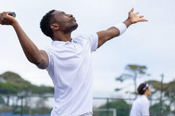 Diverse tennis players serving on tennis court with racket, wristband, chain-link fence, copy space