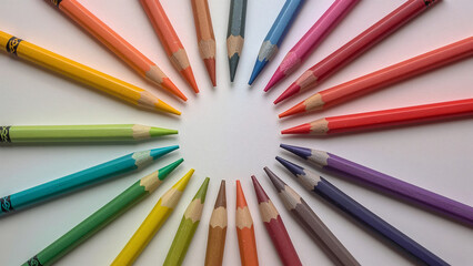 Fototapeta premium image of wax crayons in bright primary and secondary colors arranged radially. Matte white background with faint shadows adds a playful, precise, creative art-school aesthetic.