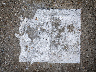 A worn and partially dissolved piece of white paper stuck to a gritty concrete surface. 