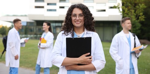 Medical student in uniform with clipboard outdoors, selective focus