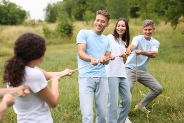 Fototapeta premium Team building. Group of happy people playing tug of war with rope outdoors