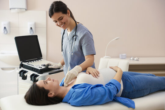 Sonographer conducting ultrasound examination of pregnant woman's thyroid gland in clinic