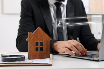 Searching for housing online. Real estate agent using laptop at table with magnifying glass and house model, closeup. Search bar above computer