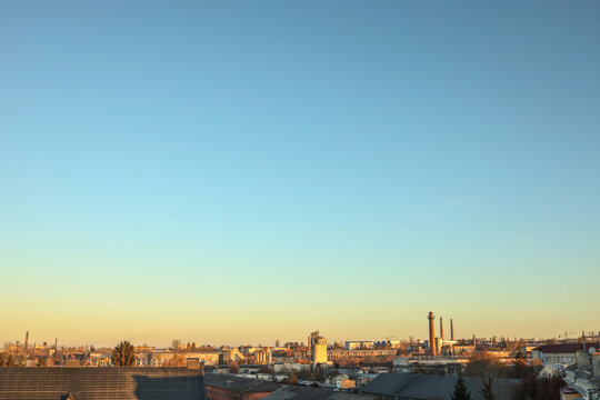 Cityscape view with industrial buildings and rooftops under a clear blue sky during golden hour, creating a calm and warm urban atmosphere - Powered by Adobe