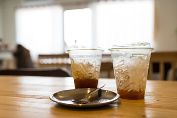 Two glass of black coffee and ice with a little left placed together with empty dessert dish after eating at cafe