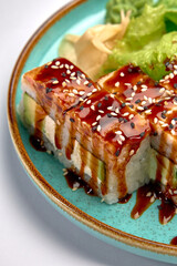 Delicious sushi rolls with rich eel sauce, sesame seeds, and fresh greens served on a vibrant turquoise plate, perfect for food lovers and culinary enthusiasts.