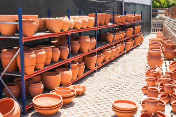 Terracotta pots of different shapes and sizes are neatly arranged on blue and red metal shelves at an outdoor garden supply area.