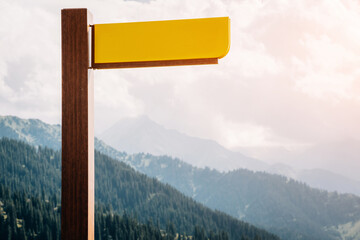 Empty yellow signage offering ample copy space for text, positioned against a stunning mountain landscape filled with lush greenery and blue skies