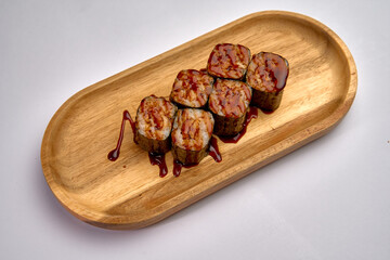 Delicious sushi rolls served on a wooden platter, drizzled with savory sauce, showcasing the blend of fresh ingredients and culinary artistry.
