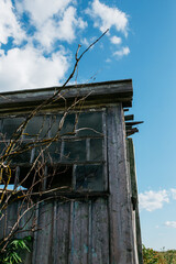 An old wooden abandoned house with broken windows stands in a field among overgrown grass on a summer day against a clear and clear blue sky with clouds. the texture of an old house