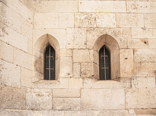 Medieval stone wall with two narrow arched windows protected by metal bars