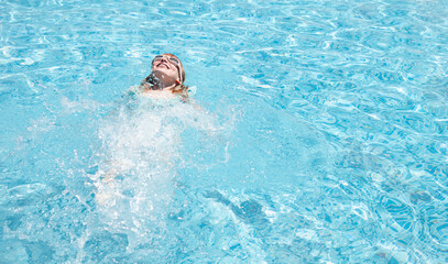 Smiling girl swimming on back in pool with goggles, blue water background, copy space. Happy child girl floating on back in blue pool. Summer vacation, resort, swimming lessons, healthy lifestyle