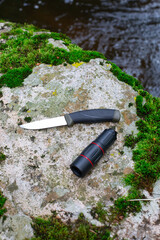 camping knife and monocular on a stone near a river