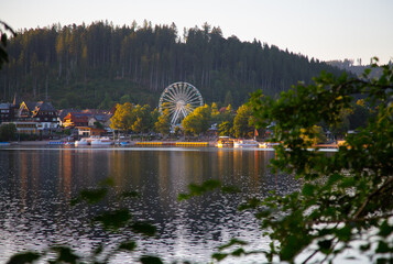 view on the lake coast with Ferris wheel and mountain forest at sunset