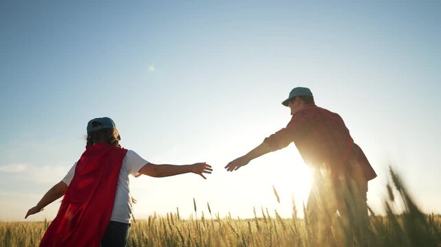 Family playing superhero in wheat field. Child wearing red cape imagines being hero. family bonding time in nature. Wheat field adventure with superhero theme. Family creating heroic memories together - Powered by Adobe