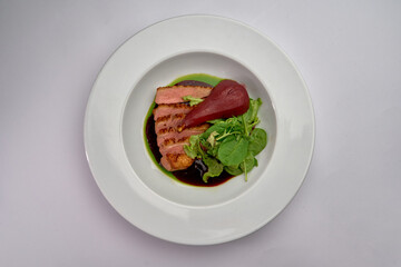 A Gourmet Dish Featuring Succulent Slices of Duck with a Side of Fresh Greens and Poached Pear in a Rich Sauce on a White Plate