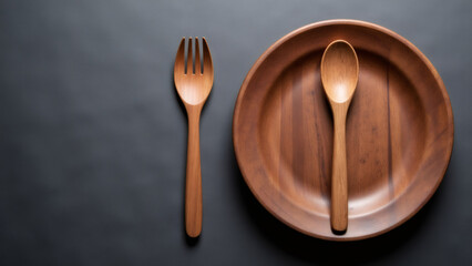 Wooden fork, spoon, and plate on a dark gray surface, flat lay.
