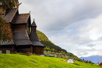 Fototapeta premium Hopperstad Stavkyrkje in South Norway, a historic wooden church surrounded by autumn trees and a peaceful graveyard.
