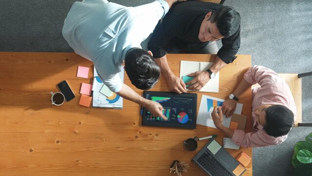 Top aerial view of diverse business team talking and brainstorming marketing idea while colleague walking and joining meeting. Professional people solving problem and looking at report. Convocation.